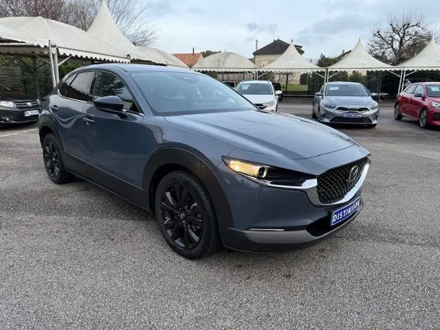 Vue 3/4 avant d'un Mazda CX-30 2024 Polymetal Grey avec jantes noires et calandre distinctive en concession.