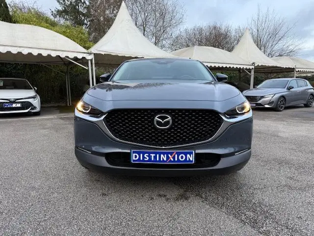 Vue frontale d'un Mazda CX-30 2.5 E-SKYACTIV-G M-HYBRID 140 Homura en Polymetal Grey avec phares allumés.