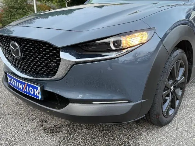 Vue avant droite d'un Mazda CX-30 2024 gris Polymetal avec phare allumé et calandre noire texturée.