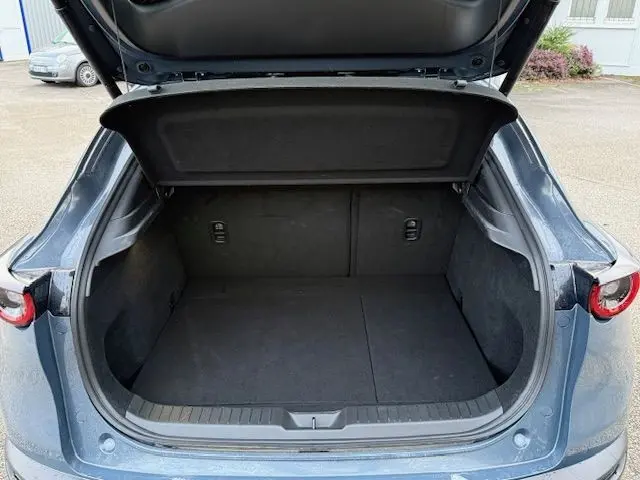 Coffre ouvert vu de l'arrière d'un Mazda CX-30 2024 gris Polymetal, montrant un espace de chargement vide et propre.