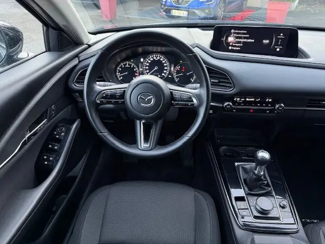 Vue intérieure centrée sur le volant et tableau de bord du Mazda CX-30 gris, avec boîte manuelle et écran multimédia.