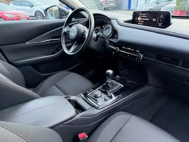 Vue intérieure côté conducteur de la Mazda CX-30 2024 gris Polymetal, avec tableau de bord moderne et boîte manuelle.
