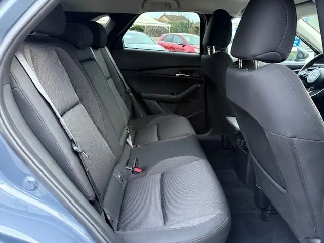 Vue intérieure arrière côté gauche du Mazda CX-30 2024, sièges tissu gris foncé avec surpiqûres rouges, porte ouverte.