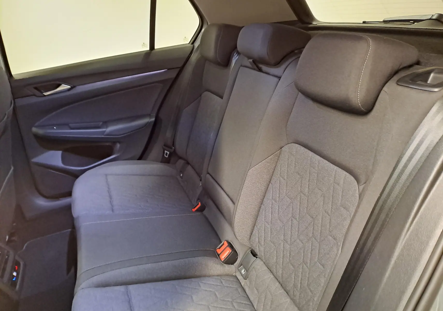 Vue intérieure du siège arrière droit de la Volkswagen Golf 1.5 TSI 2025 avec tissu gris et ceintures de sécurité visibles.