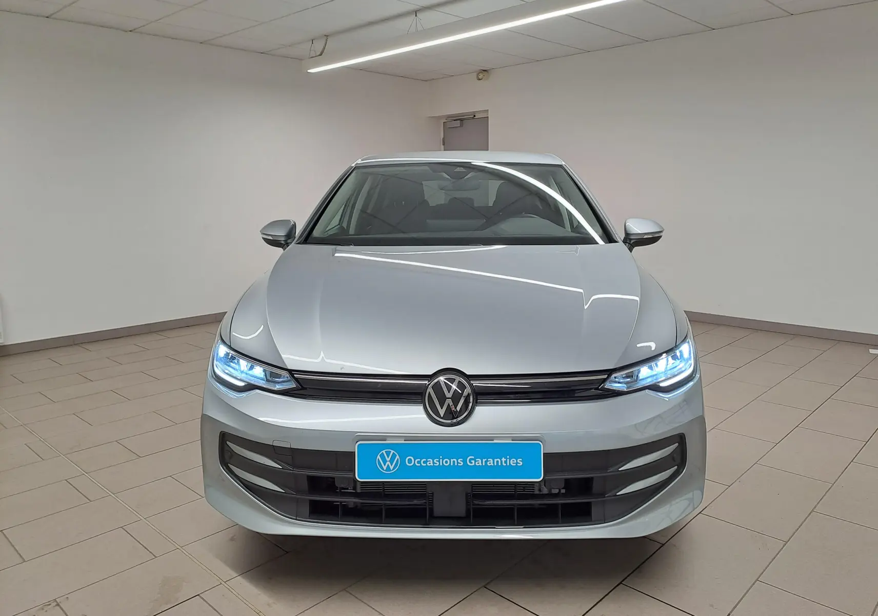 Vue frontale d'une Volkswagen Golf 1.5 TSI 116 BVM6 VW Edition en argent Dolomite avec phares LED allumés.
