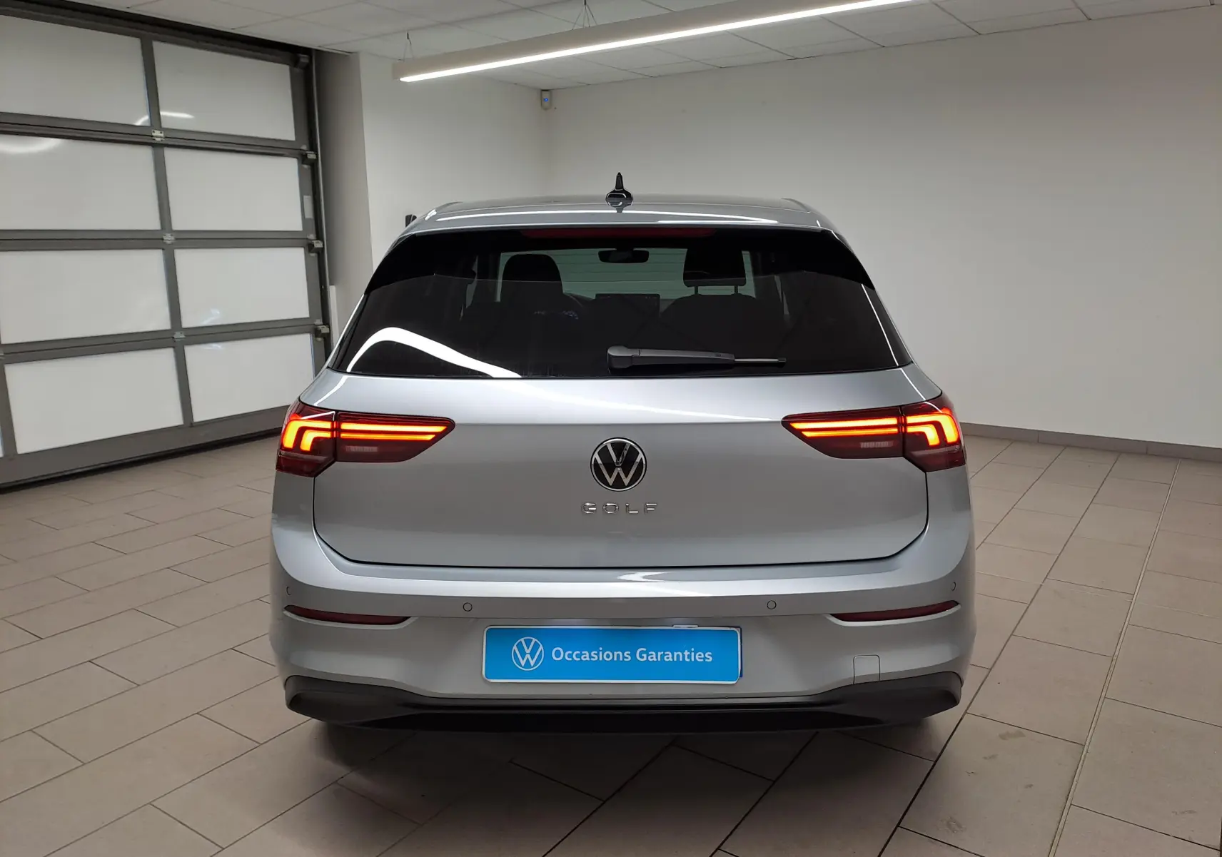 Vue arrière d'une Volkswagen Golf 1.5 TSI 116 BVM6 argent Dolomite avec feux allumés dans un garage.