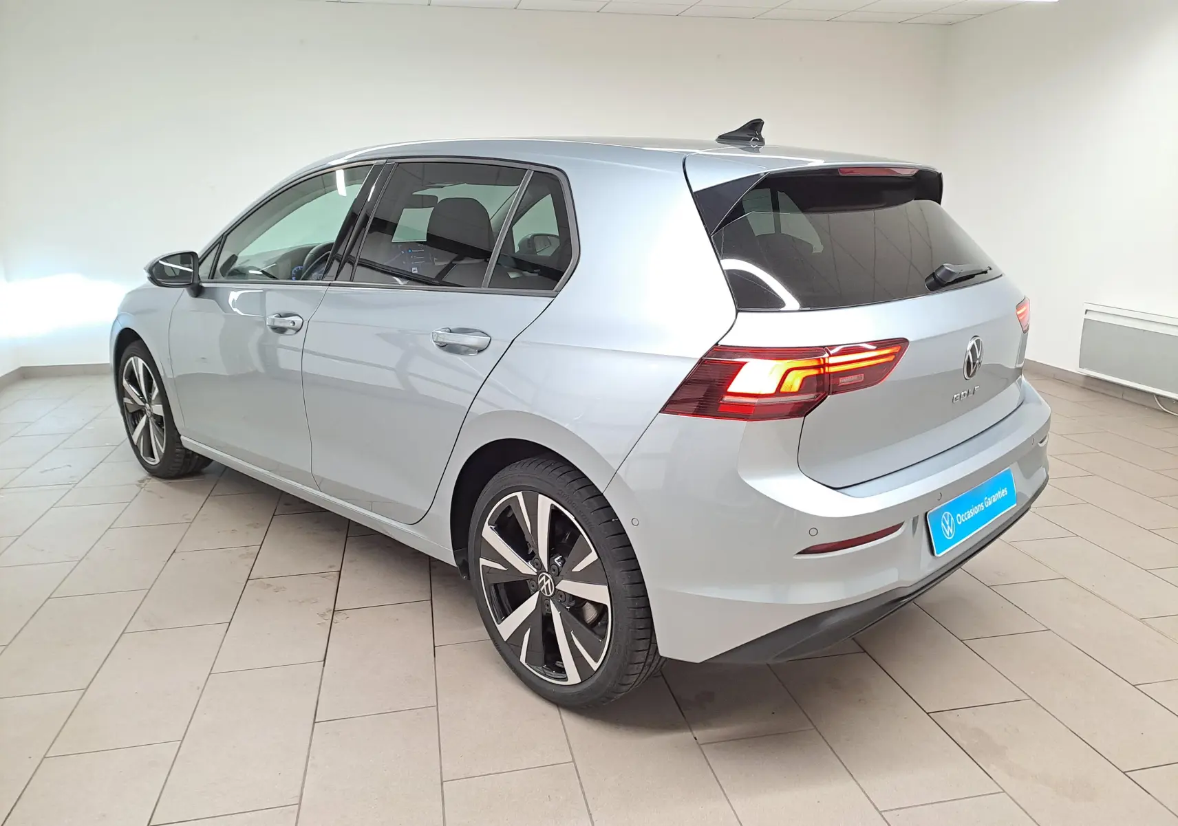 Volkswagen Golf 1.5 TSI 2025 vue 3/4 arrière côté gauche, peinture argent Dolomite et jantes alliage 18 pouces.