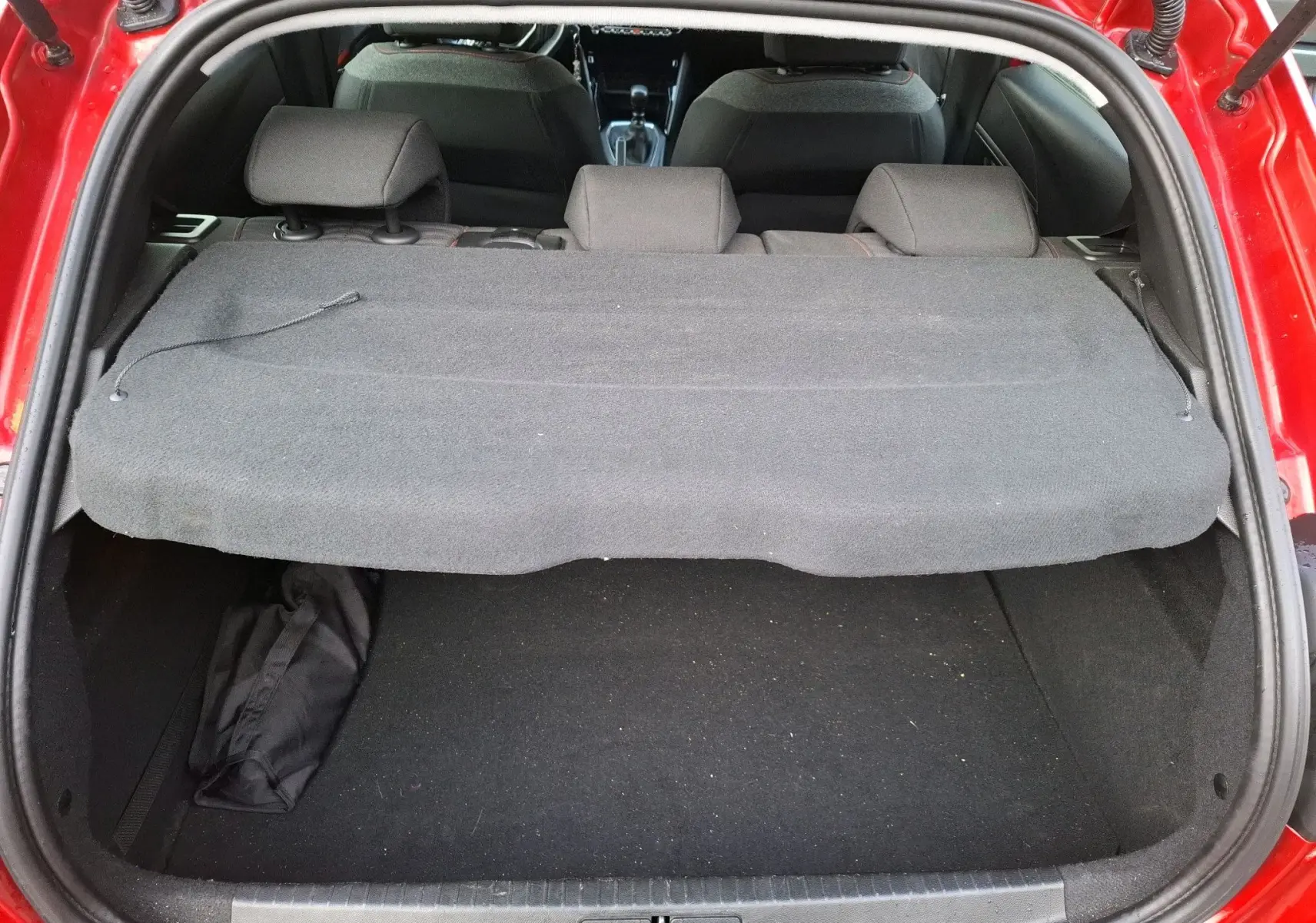 Vue arrière du coffre ouvert d'une Peugeot 208 rouge Elixir, avec cache-bagages en place et sièges arrière visibles.