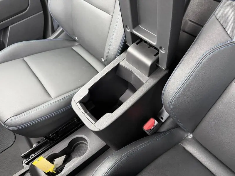 Vue rapprochée de l'accoudoir central ouvert et des sièges noirs avec surpiqûres bleues dans le Nissan Townstar blanc Minéral 2024.