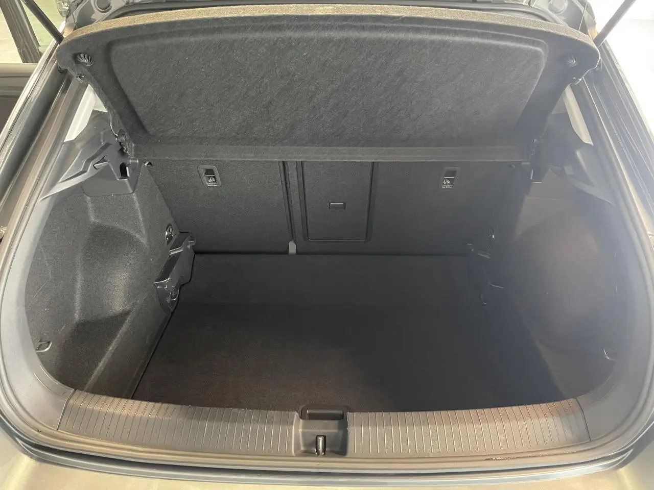 Coffre ouvert vu de l'arrière d'un Volkswagen T-Roc 2025 gris Indium, intérieur noir et moquette propre.