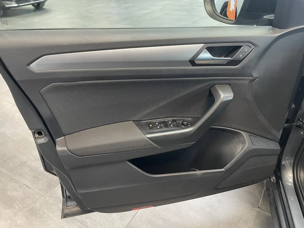 Vue rapprochée de la porte avant gauche du Volkswagen T-Roc Indium Gray, avec commandes électriques et insert argenté.