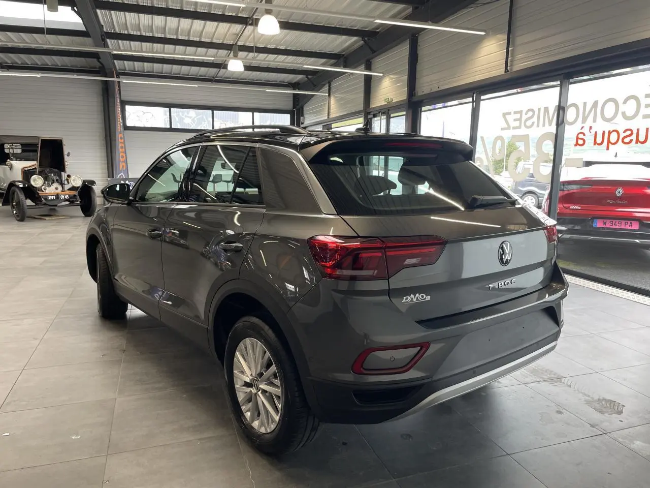 Volkswagen T-Roc gris Indium vu en 3/4 arrière droit avec toit noir et jantes alliage 16 pouces en showroom.
