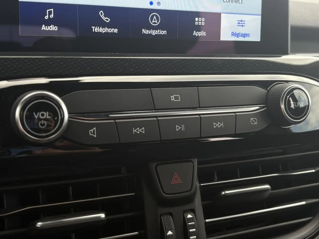 Gros plan sur la console centrale du Ford Kuga 2023, boutons audio et ventilation avec écran tactile en haut.