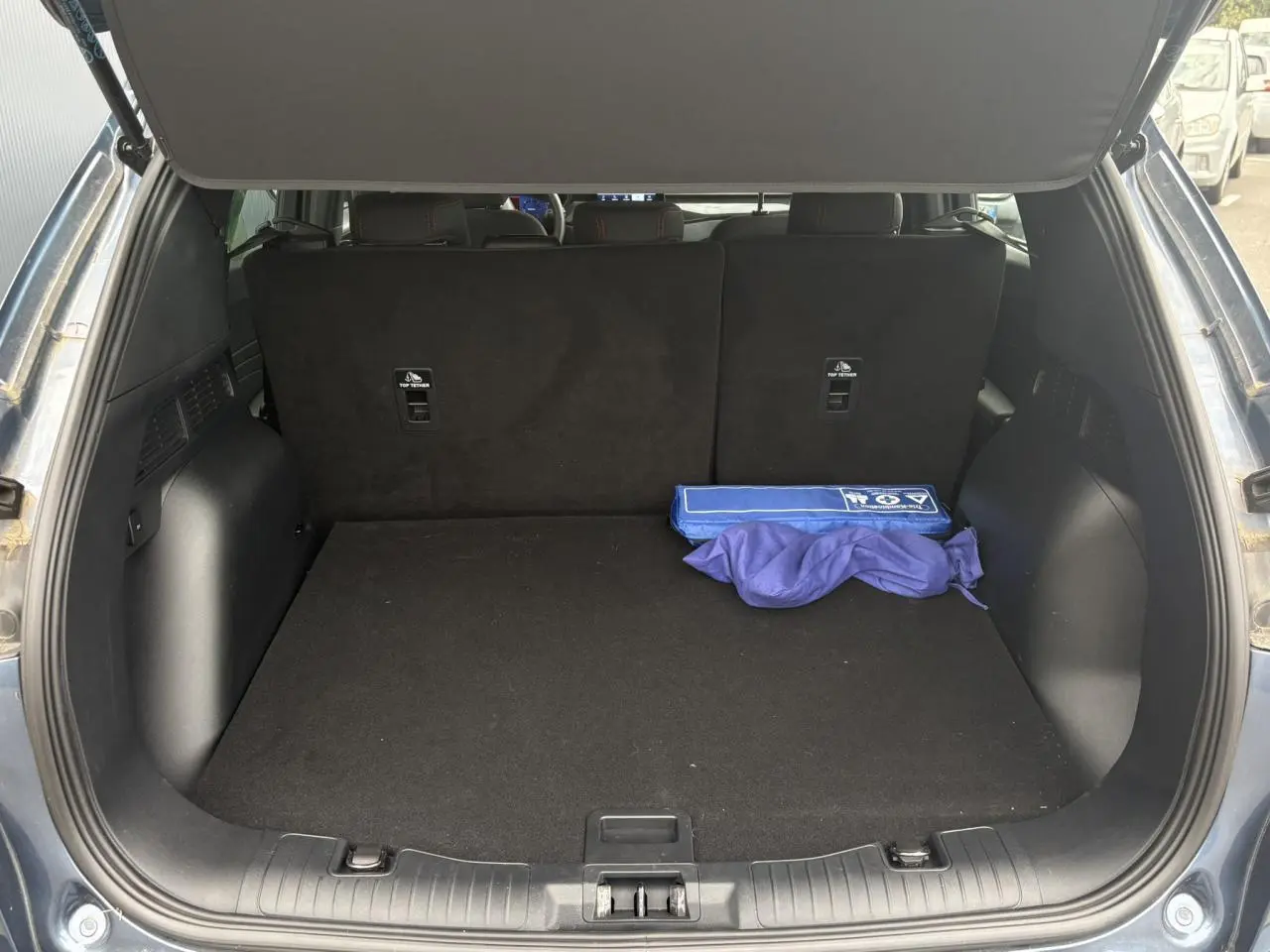 Coffre ouvert d'un Ford Kuga gris azur 2023, montrant l'espace de chargement avec un kit de sécurité bleu.