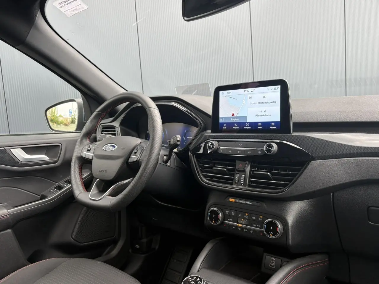 Vue intérieure côté conducteur du Ford Kuga gris azur 2023, avec volant ST-Line à surpiqûres rouges et écran tactile central.