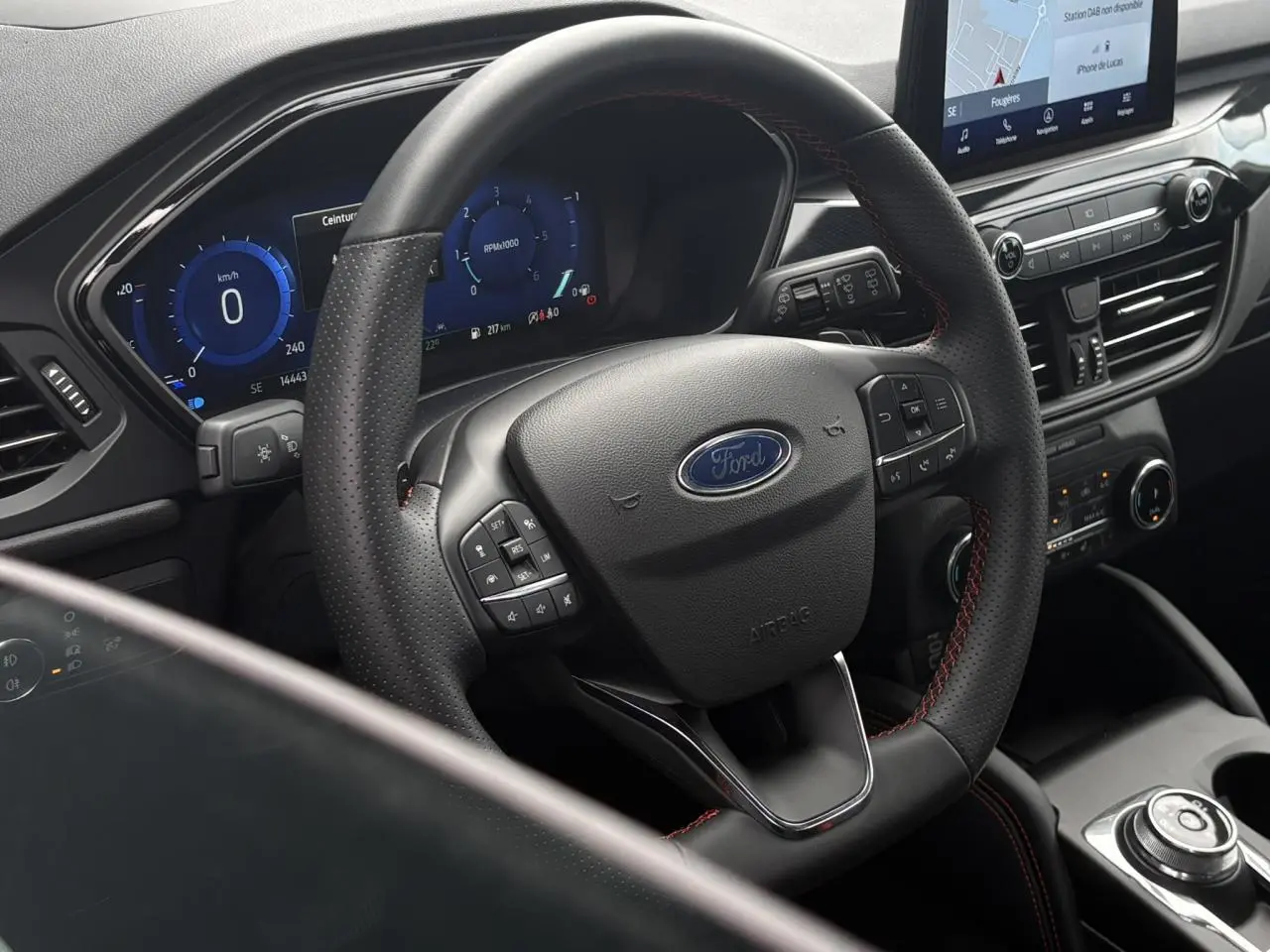 Vue rapprochée du volant cuir noir avec surpiqûres rouges et tableau de bord numérique du Ford Kuga 2023.