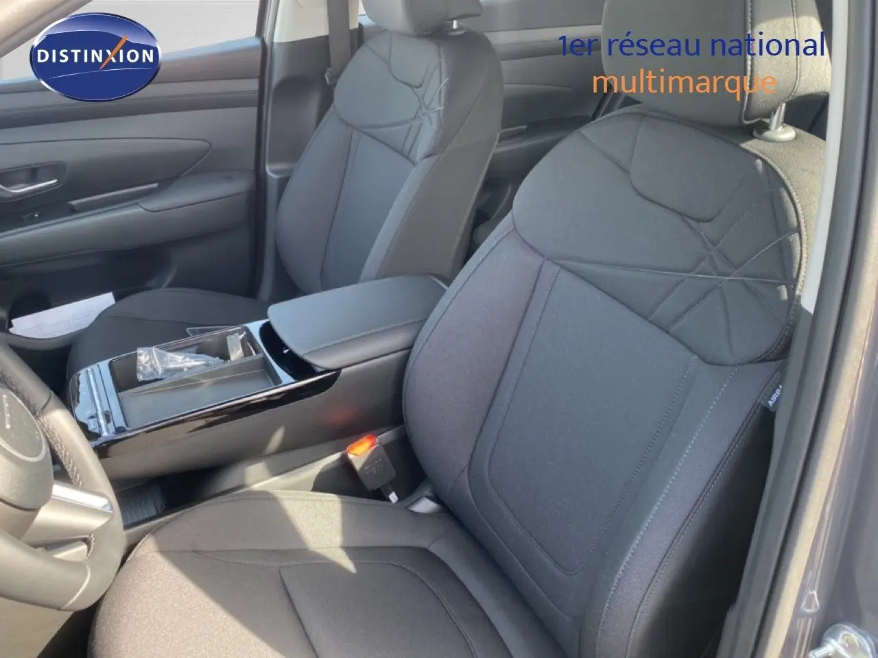 Vue intérieure côté conducteur du Hyundai Tucson 2026 gris Ecotronic, sièges tissu noir avec console centrale brillante.