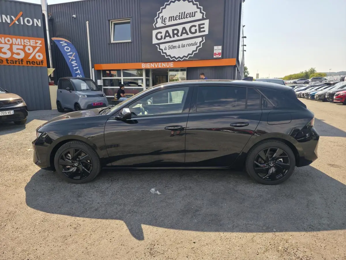 Opel Astra Hybrid 2024 noir profil côté gauche avec jantes alliage noires et vitres surteintées, stationnée devant un garage.