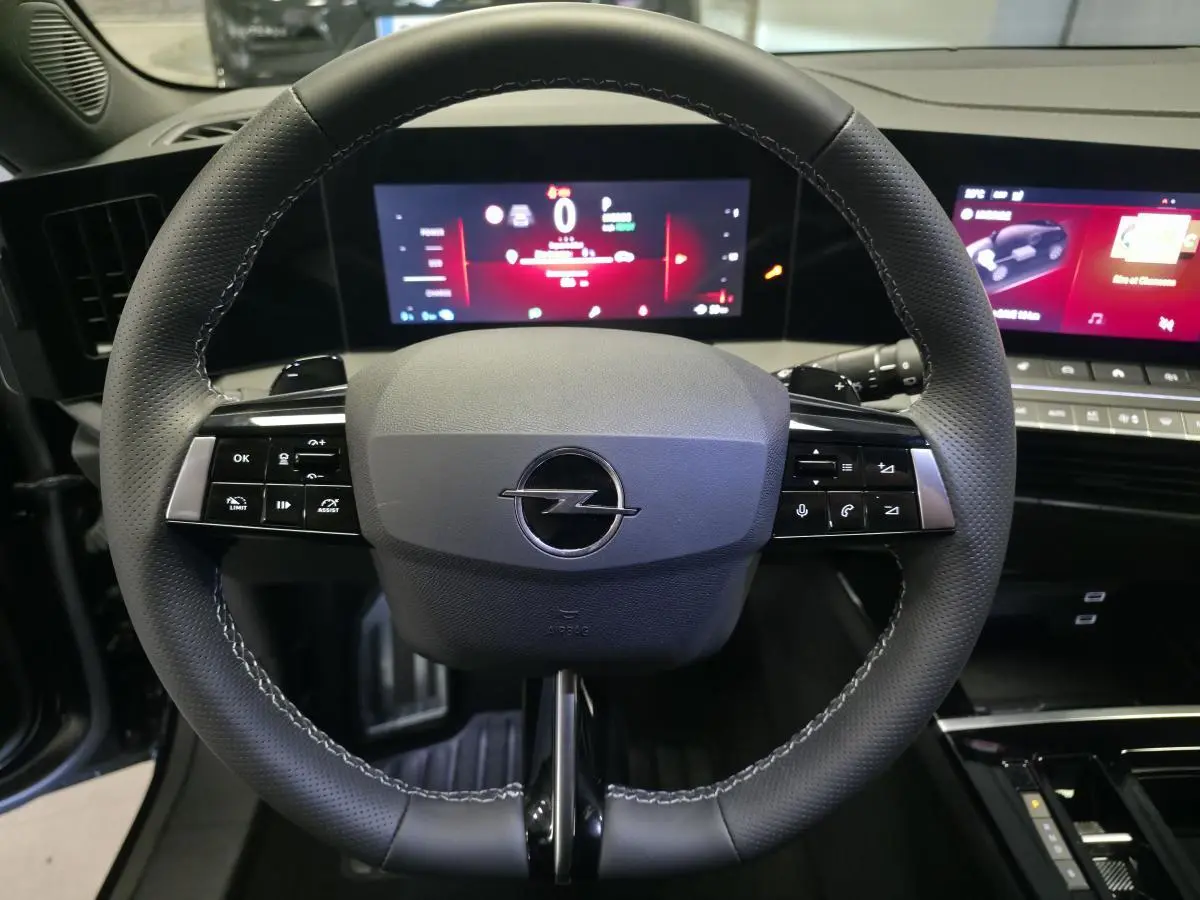 Vue rapprochée du volant noir perforé de l’Opel Astra Hybrid 2024 avec tableau de bord digital et écran tactile.