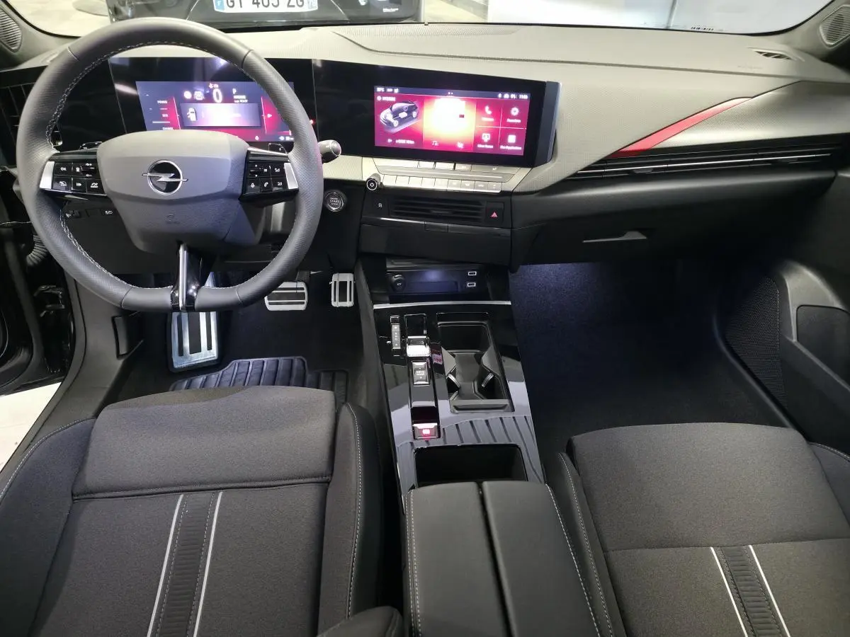 Intérieur avant de l’Opel Astra Hybrid 2024, vue du conducteur, tableau de bord noir avec écran tactile large et détails rouges.