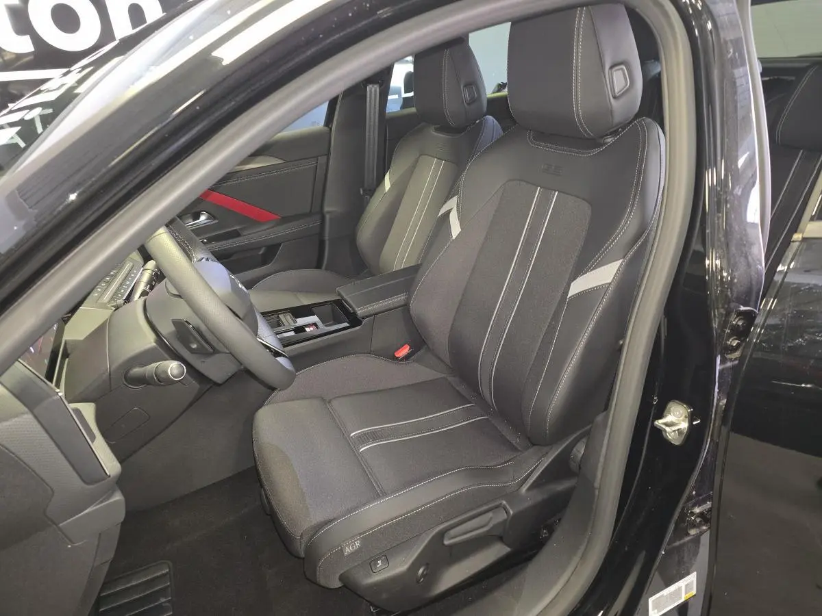 Vue intérieure côté conducteur de l’Opel Astra Hybrid 2024 noire, sièges tissu/TEP avec surpiqûres blanches et accoudoir central.