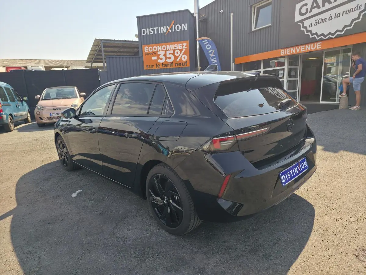 Vue 3/4 arrière droite de l'Opel Astra Hybrid noire avec jantes alliage noires et vitres surteintées.