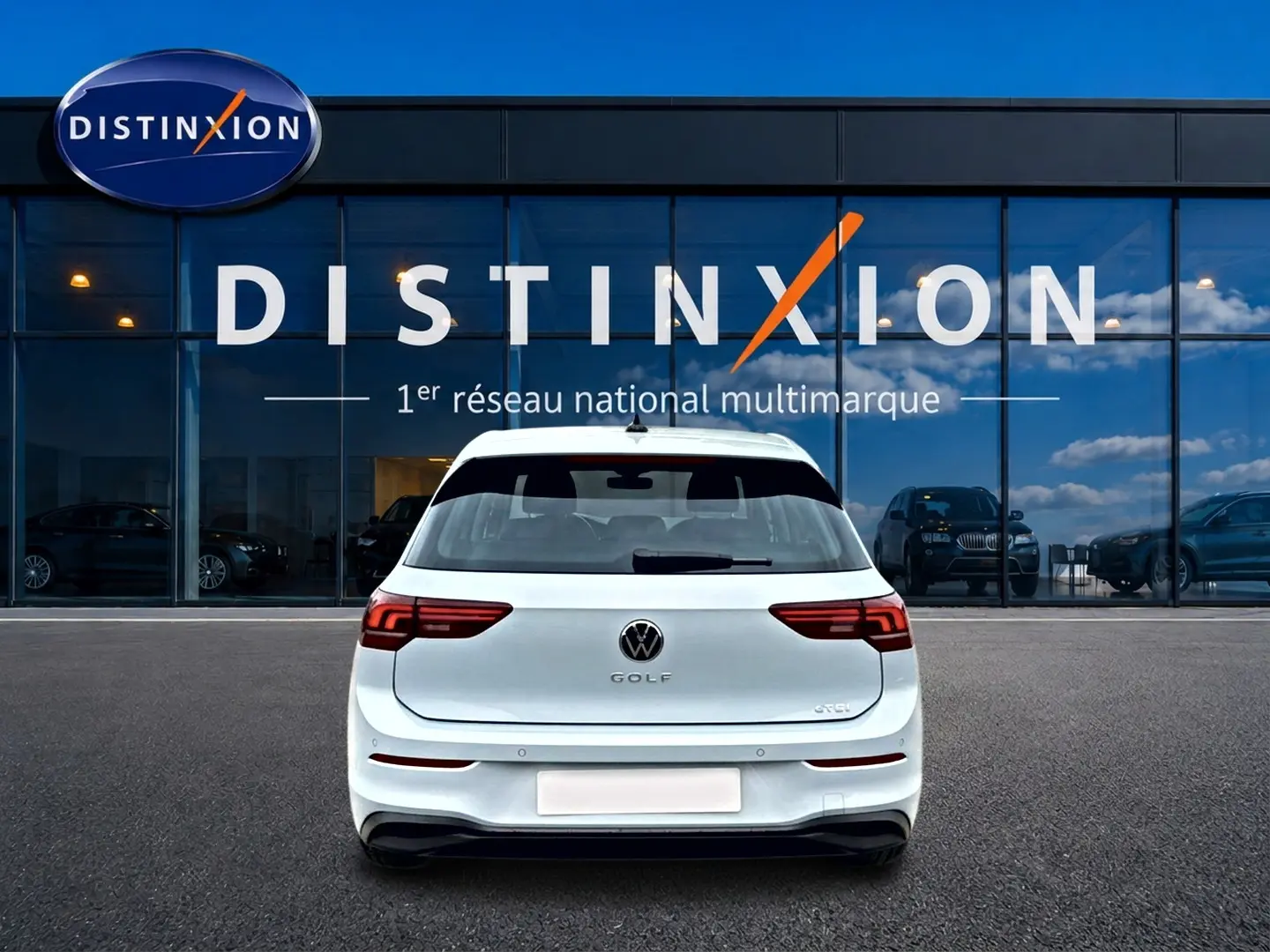 Vue arrière d'une Volkswagen Golf 1.5 etsi evo2 116 life dsg7 blanche, garée devant une vitrine Distinxion.