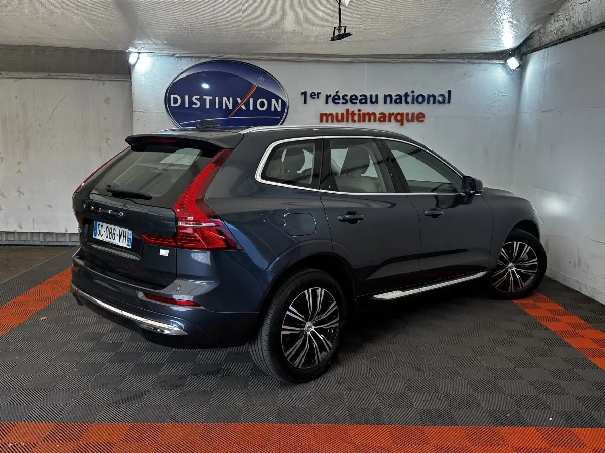 Vue 3/4 arrière droite d'un Volvo XC60 bleu hybride rechargeable avec jantes noires et toit noir dans un garage.