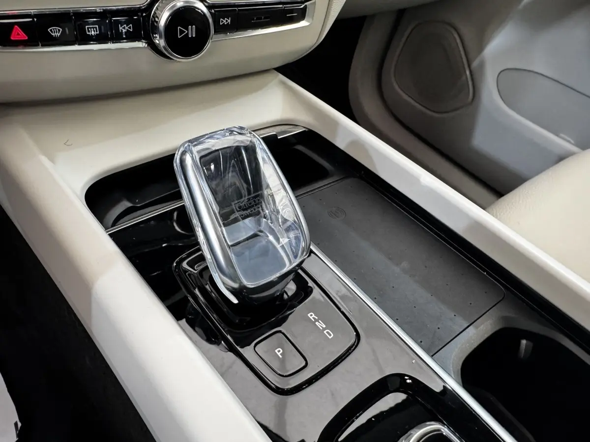 Gros plan sur la console centrale beige et noire du Volvo XC60 bleu, mettant en valeur le levier de vitesse automatique en cristal.