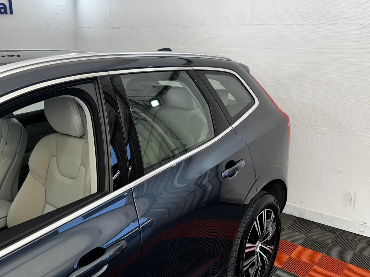 Vue latérale arrière droite d’un Volvo XC60 bleu avec sièges cuir clairs et jantes alliage noires.