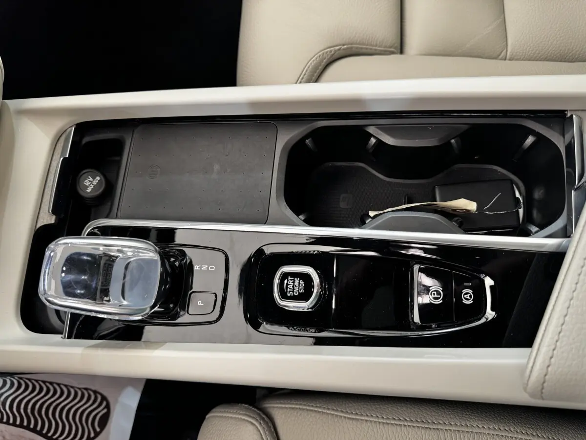 Vue rapprochée de la console centrale beige du Volvo XC60 bleu, avec levier de vitesses cristal et bouton start/stop.