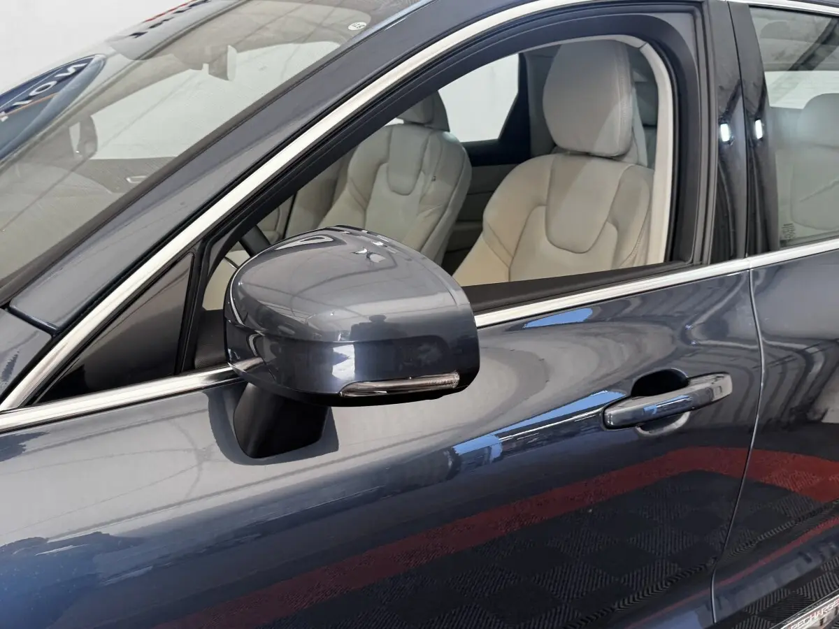 Gros plan sur le rétroviseur et la portière côté conducteur d’un Volvo XC60 bleu avec intérieur cuir beige.