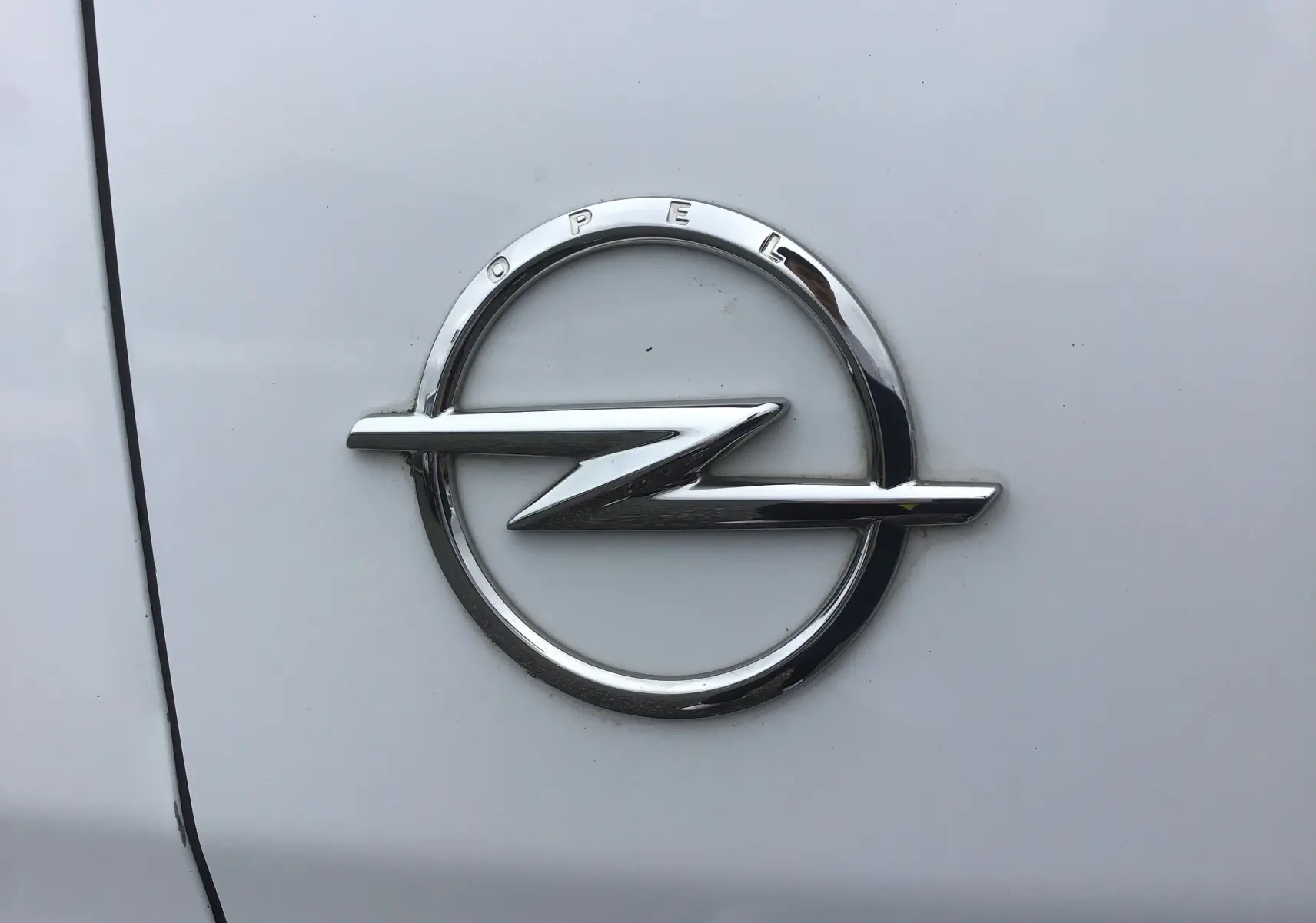 Gros plan sur l'emblème chromé Opel sur la carrosserie blanche du fourgon Vivaro M 1.5 BlueHDi 2022