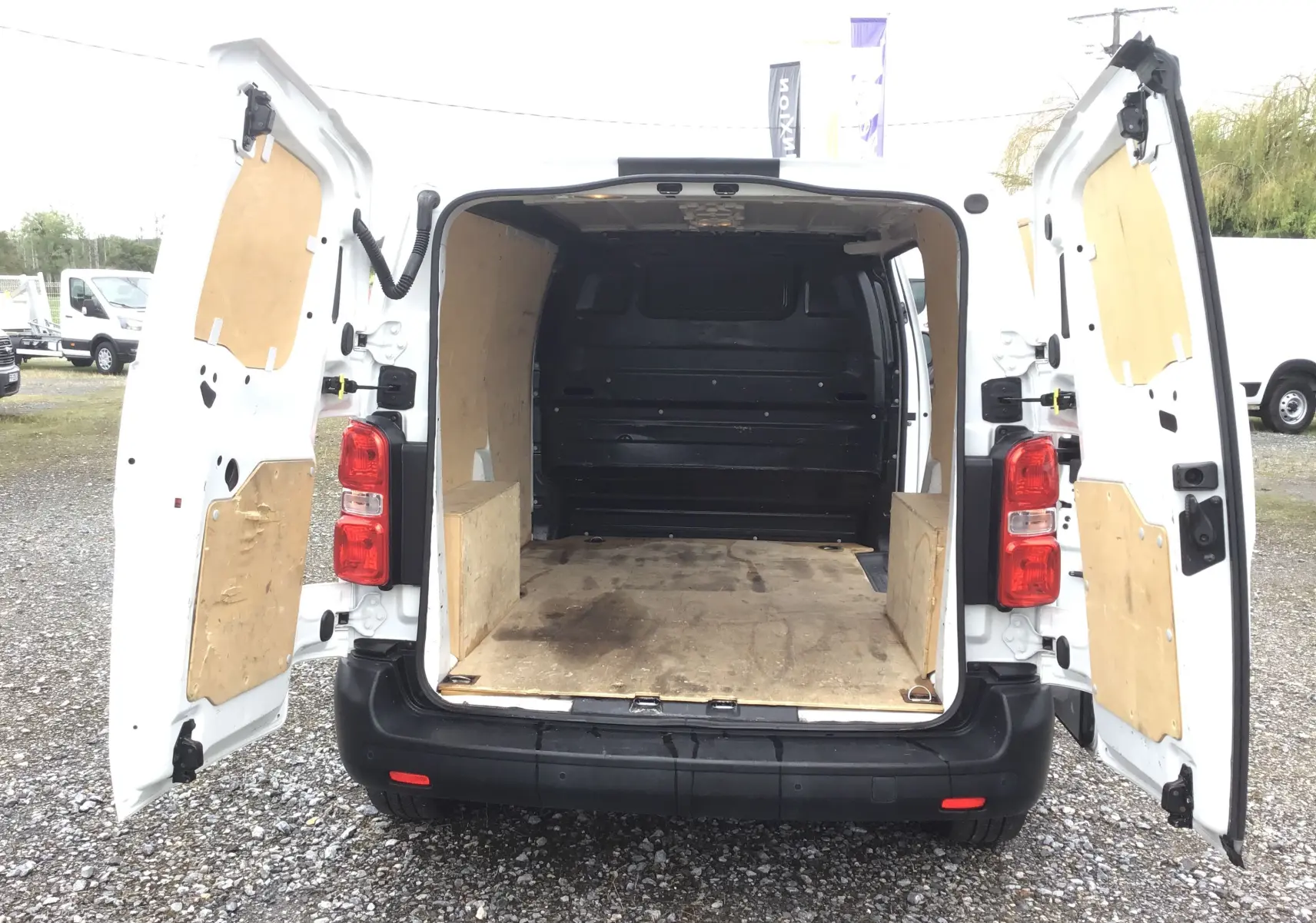 Vue arrière d'un Opel Vivaro blanc 2022 avec portes ouvertes montrant l'espace de chargement en bois.