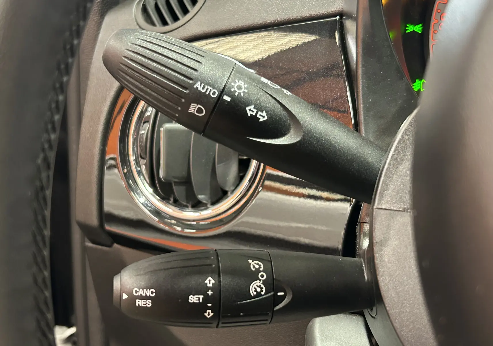 Gros plan sur les commandes de clignotants et régulateur de vitesse à gauche du volant d'une Fiat 500 noire 2023.