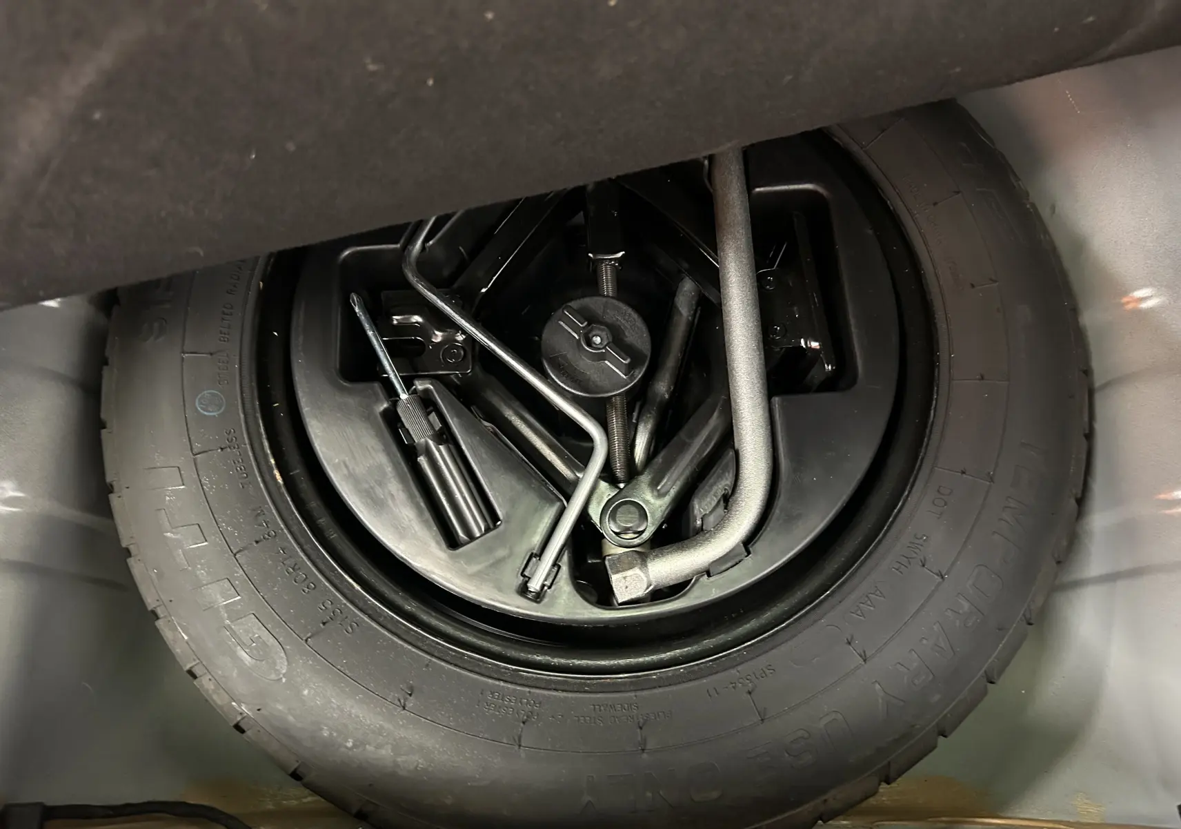 Gros plan sur la roue de secours et les outils de bord du coffre d'une FIAT 500 noire 2023.