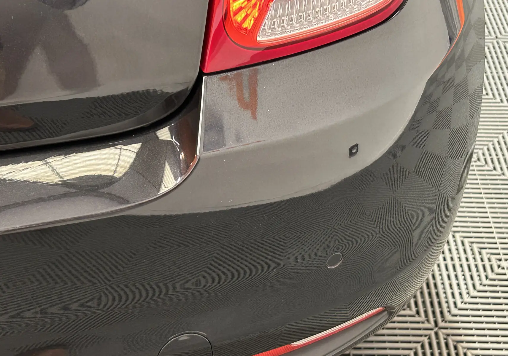 Gros plan sur le pare-chocs arrière noir d'une Fiat 500 2023, avec feu arrière et capteurs de radar de recul visibles.