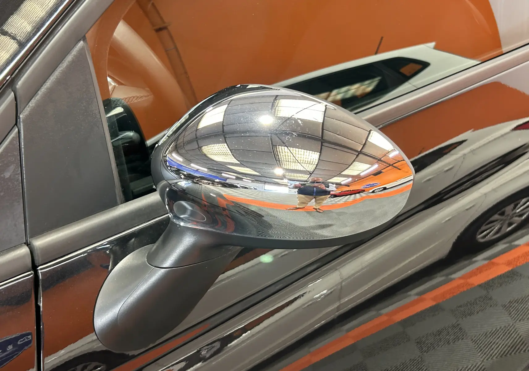 Rétroviseur chromé côté gauche d'une Fiat 500 noire 2023 avec reflet intérieur et environnement lumineux.