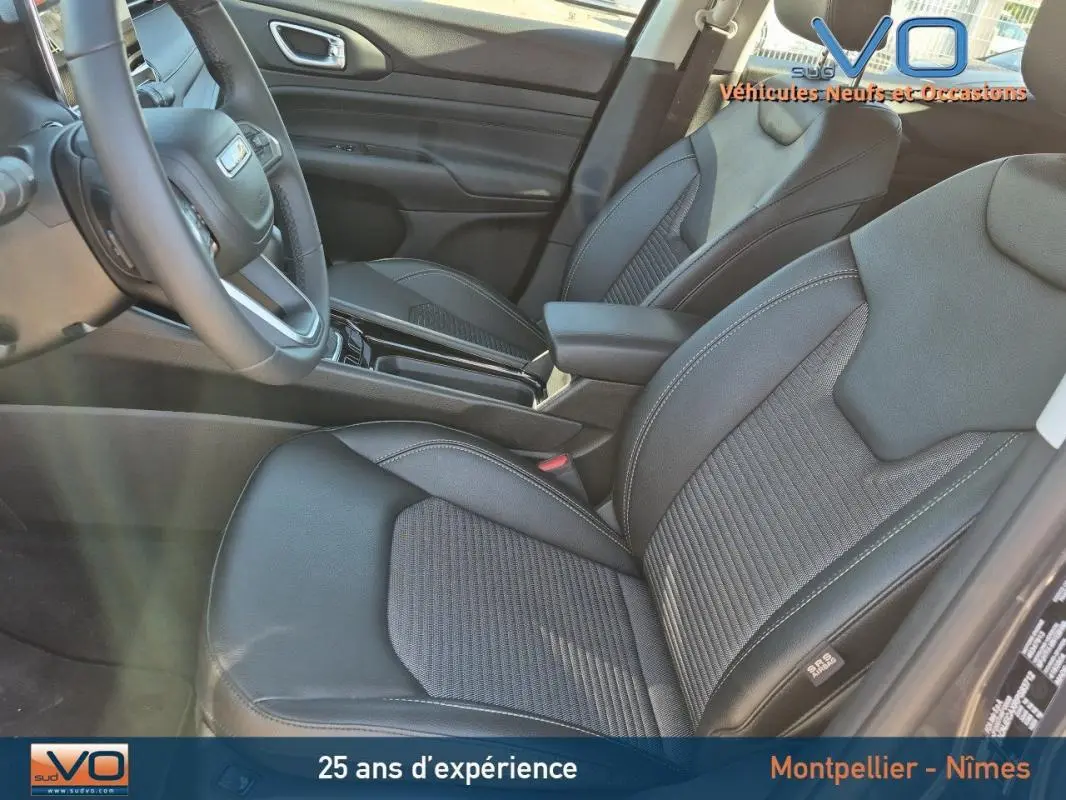 Intérieur avant du Jeep Compass gris 2024, sièges en cuir noir avec accoudoir central et volant visible côté conducteur.