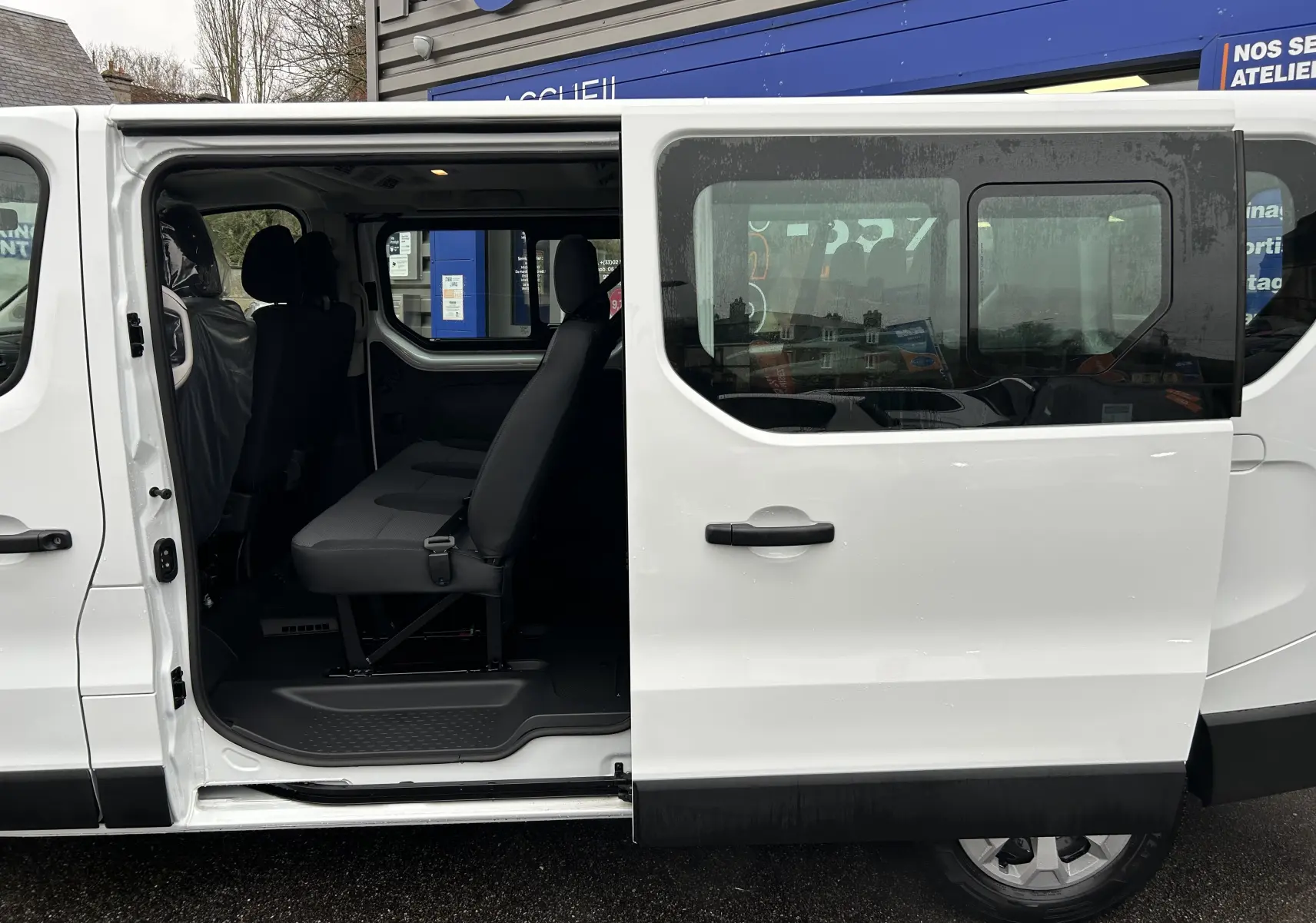 Vue latérale droite du Renault Trafic Combi blanc Glacier avec porte coulissante ouverte dévoilant la banquette arrière en tissu.