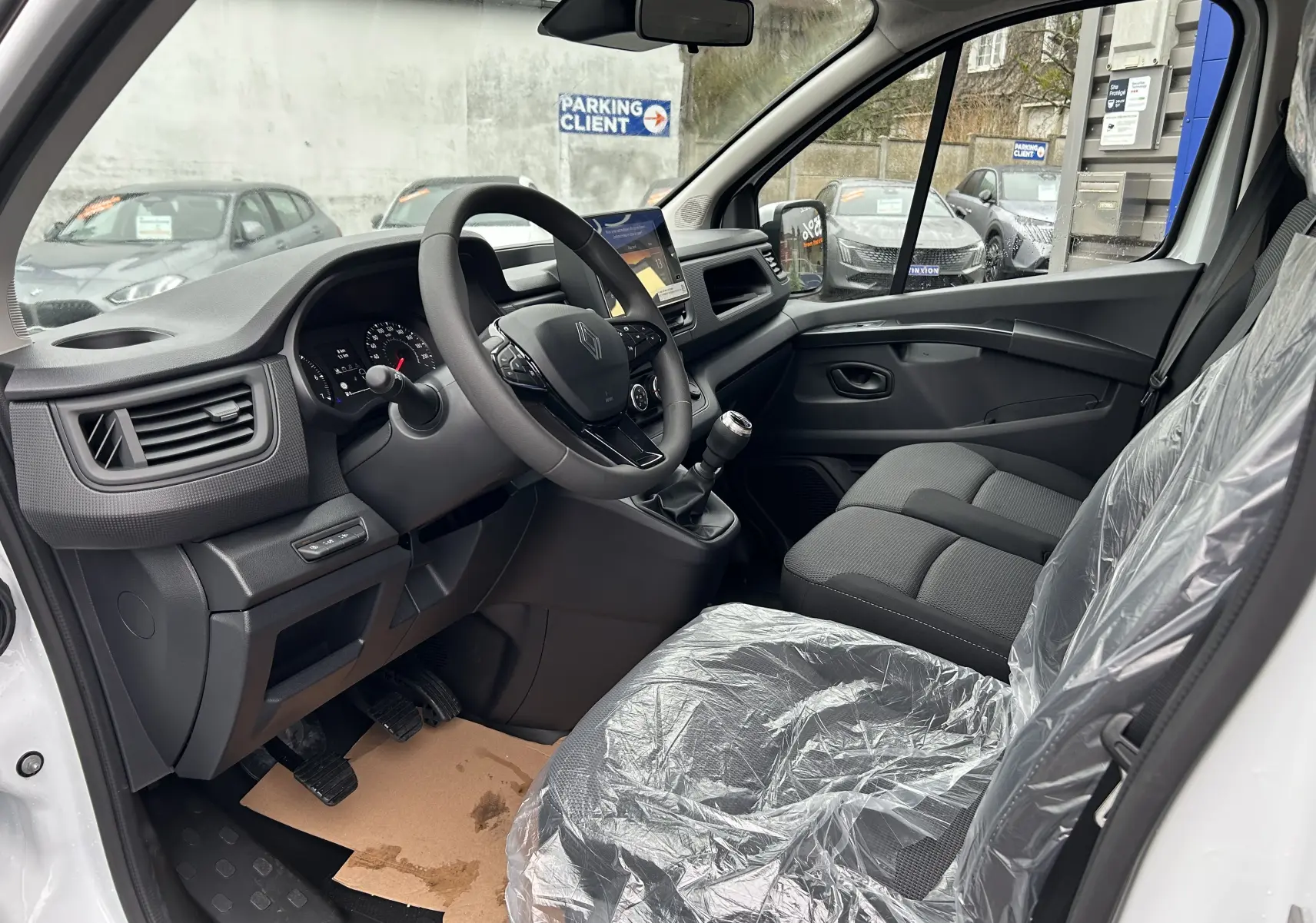 Vue intérieure côté conducteur du Renault Trafic Combi blanc Glacier 2025, montrant le volant, la console et les sièges en tissu protégés.