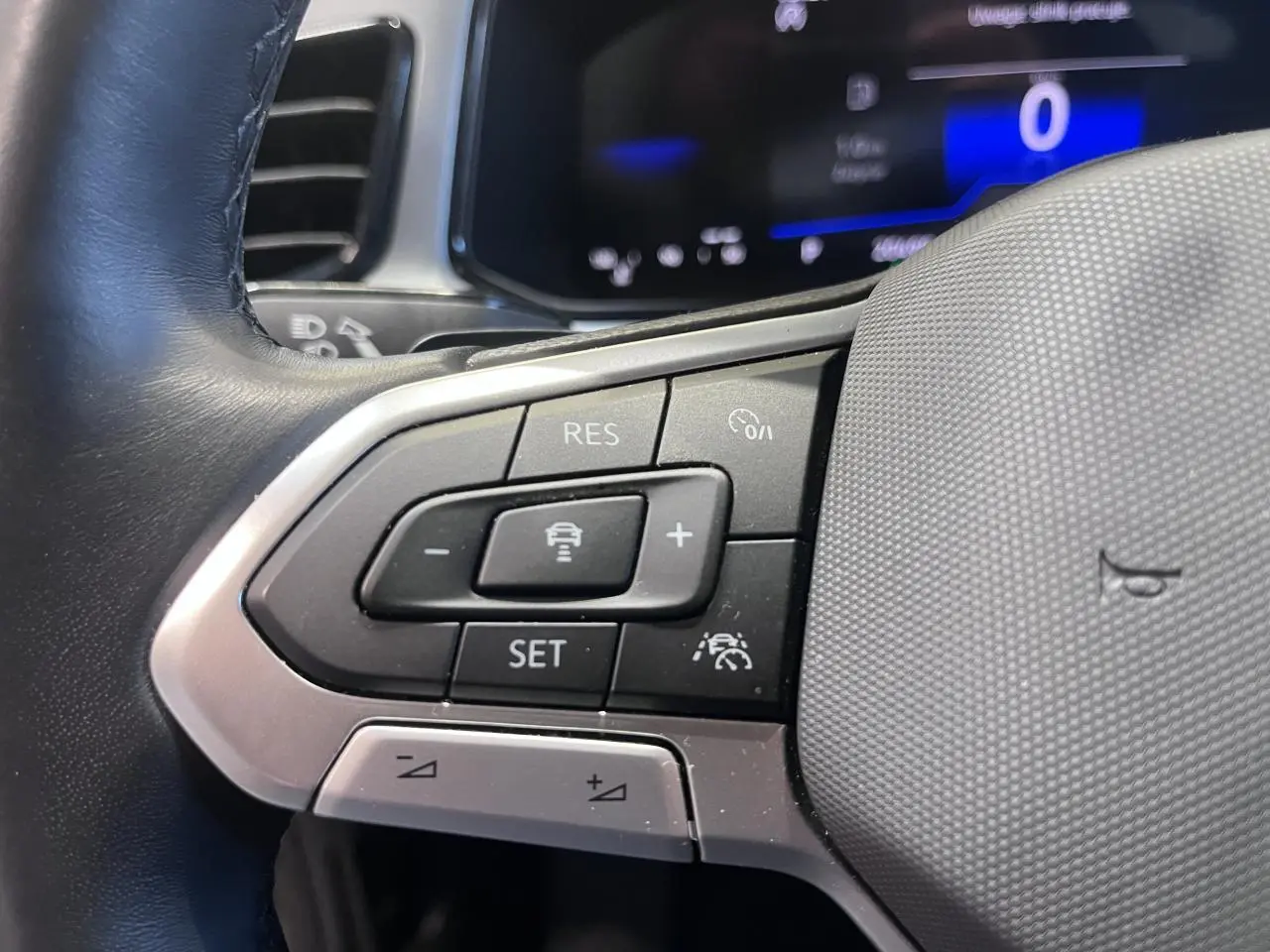 Gros plan sur les commandes au volant à gauche du Volkswagen T-Roc 2025, avec affichage digital bleu en arrière-plan.