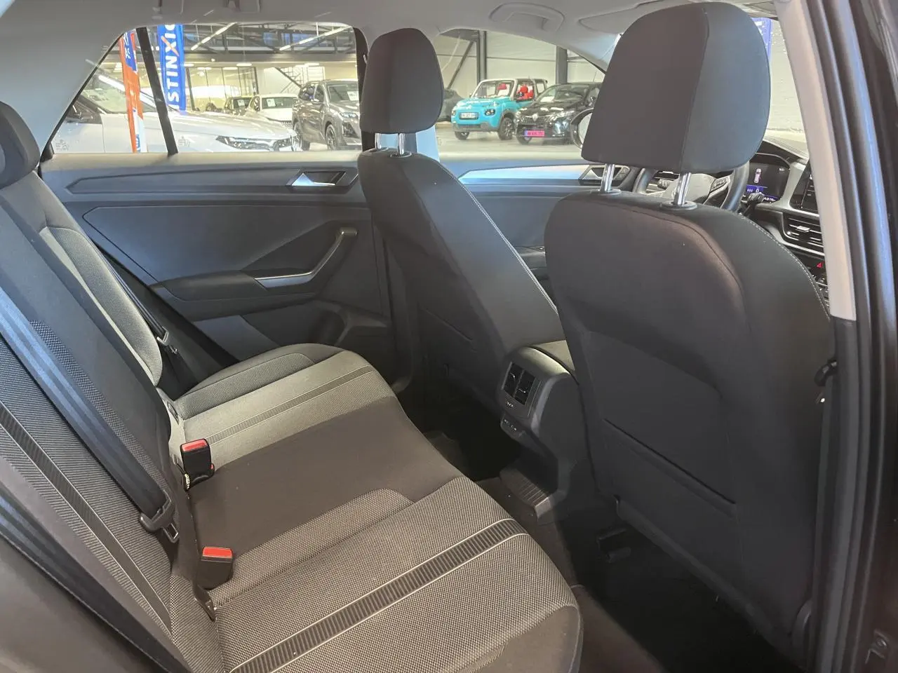 Vue intérieure arrière du Volkswagen T-Roc 2025 avec sellerie tissu noir et détails gris, montrant les sièges et aérateurs centraux.