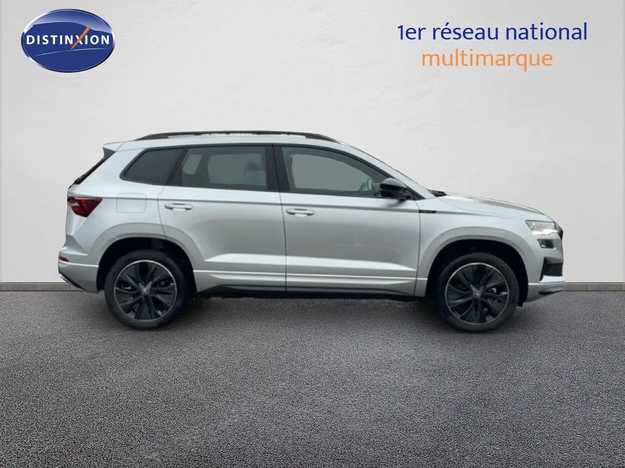 Profil droit d’un Skoda Karoq gris argent métallisé 2025 avec jantes noires et toit ouvrant panoramique.