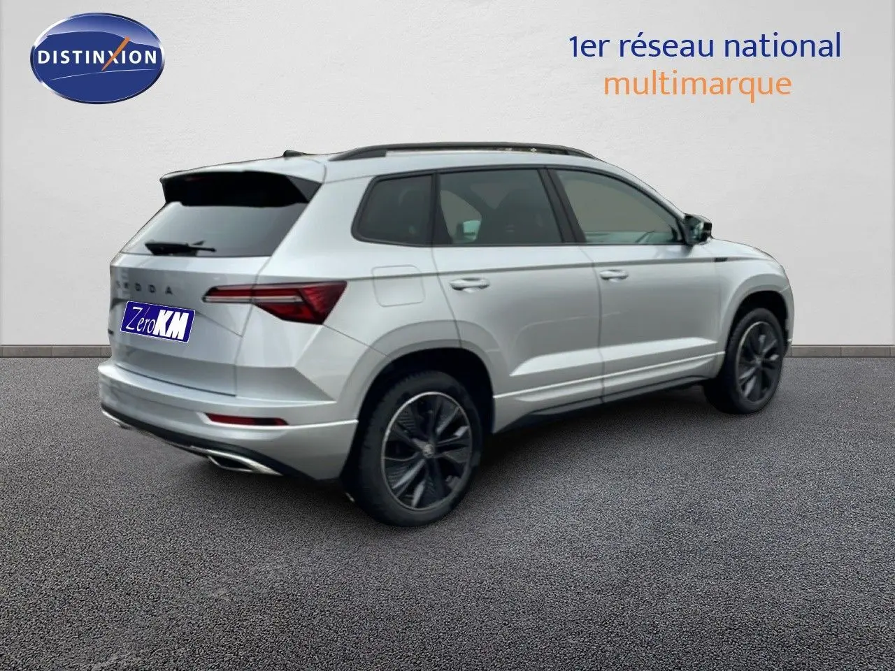 Vue 3/4 arrière droite d'un Skoda Karoq gris argent métal 2025 avec jantes noires et toit ouvrant.