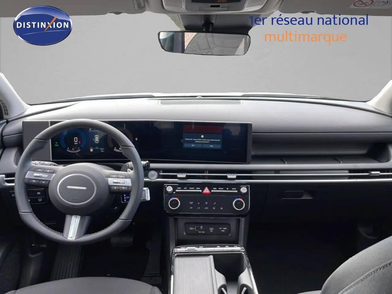 Vue intérieure avant du Hyundai Tucson blanc Atlas 2026, tableau de bord moderne avec écran large et volant multifonction noir.