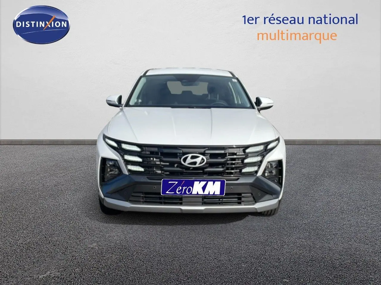 Vue frontale d’un Hyundai Tucson blanc Atlas 2026 avec calandre noire et feux LED distinctifs allumés.