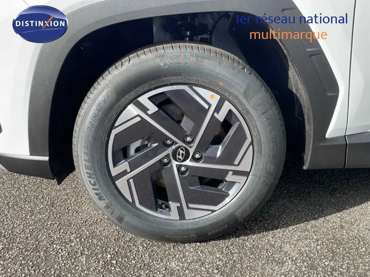 Gros plan sur la roue avant droite du Hyundai Tucson blanc Atlas, mettant en valeur la jante noire et grise au design géométrique.