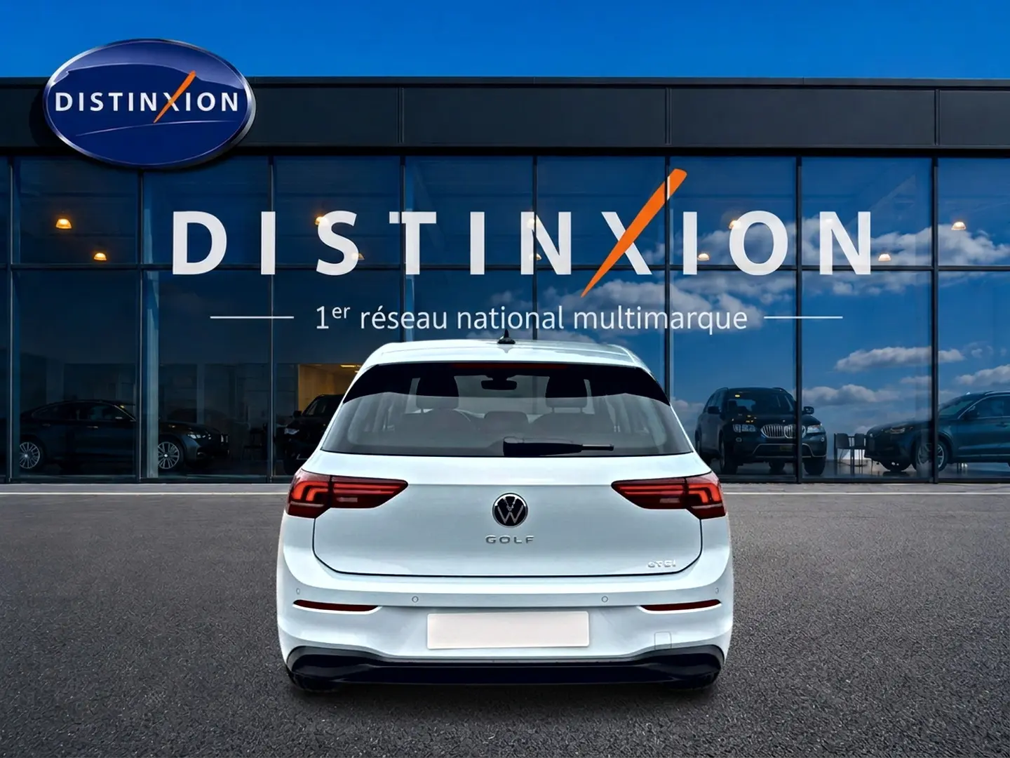 Vue arrière d'une Volkswagen Golf 1.5 etsi evo2 116 life dsg7 bleu glacier, garée devant une vitrine Distinxion.
