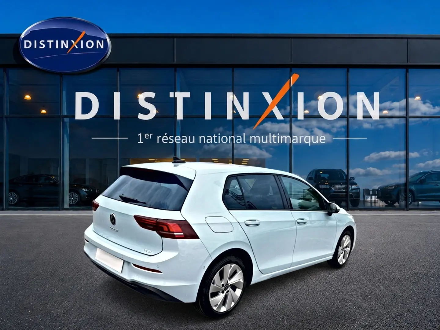 Vue 3/4 arrière droite d'une Volkswagen Golf blanche garée devant une vitrine avec logo Distinxion.